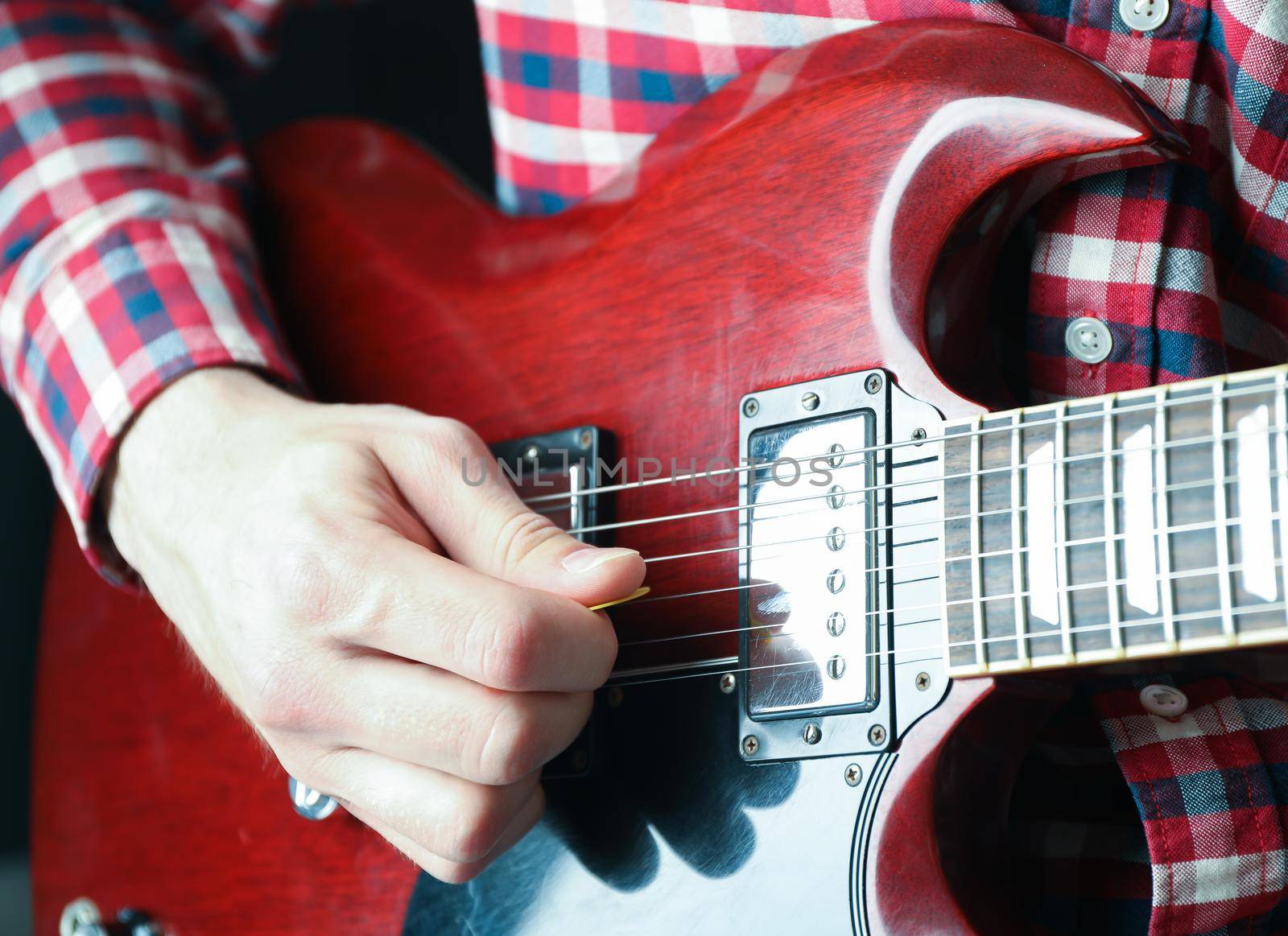 Man playing on electric guitar against dark background, closeup