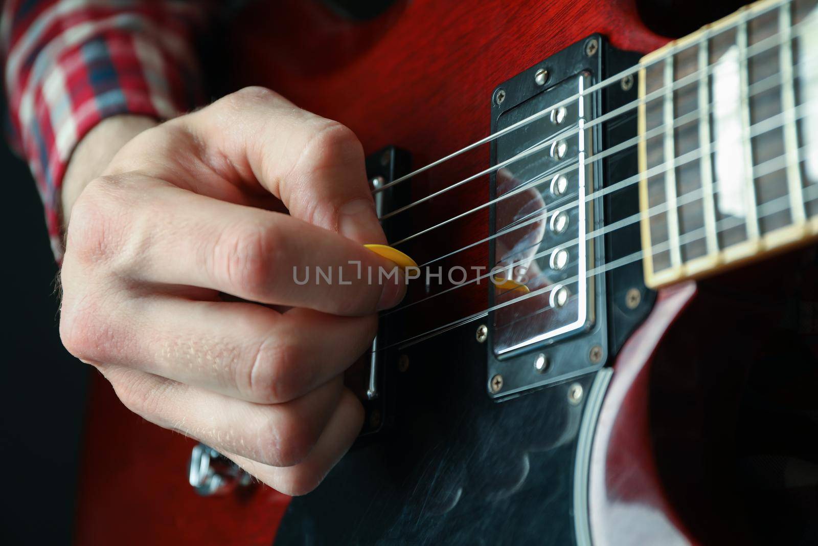 Man playing on electric guitar against dark background, closeup