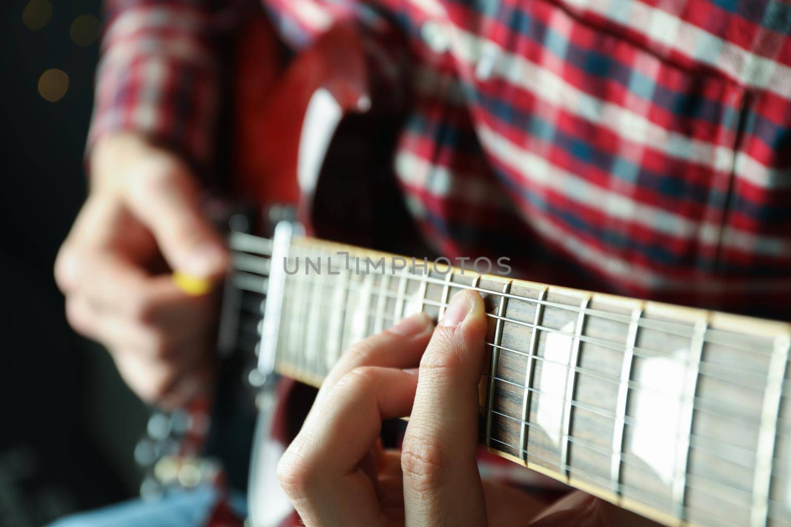 Man playing on electric guitar against dark background, closeup