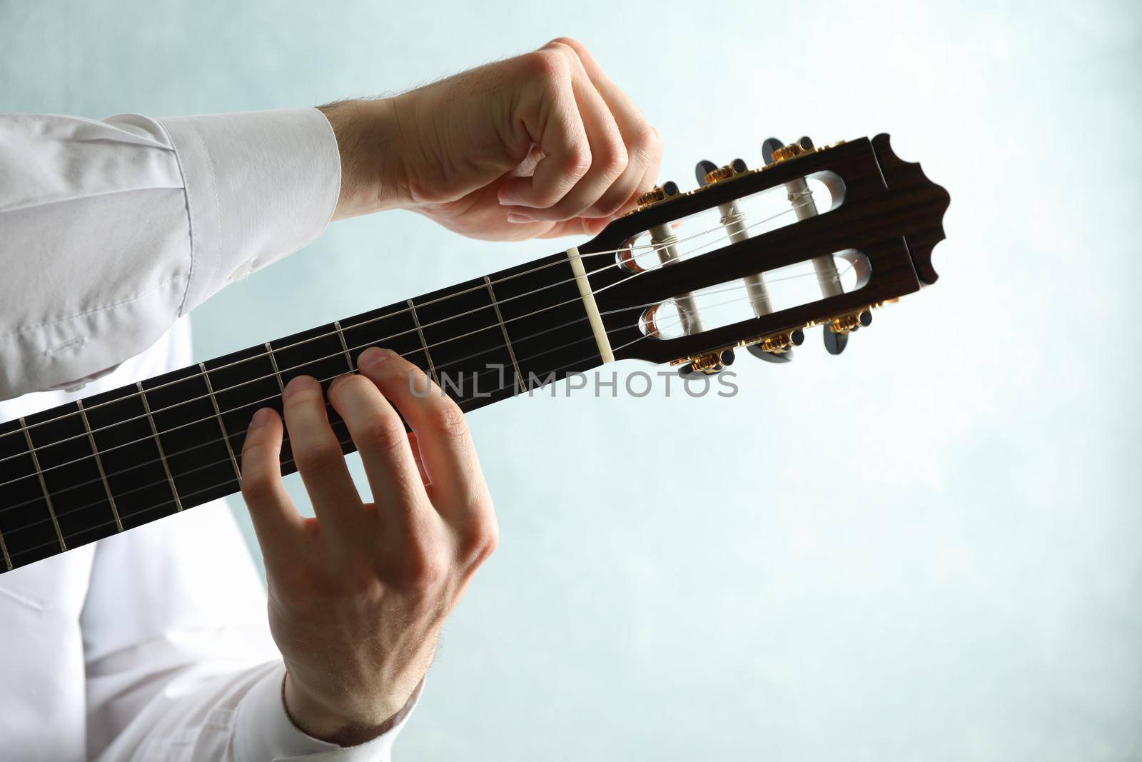 Man tunes classic guitar against light background, space for text