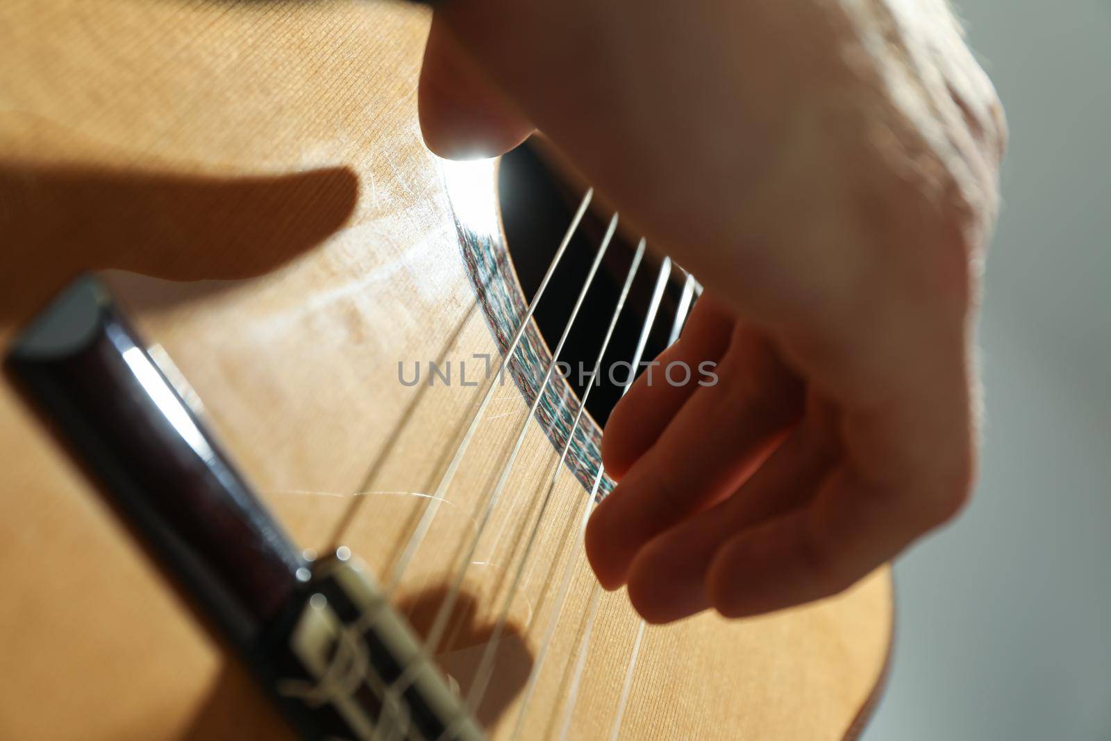 Man playing on classic guitar against light background, closeup by AtlasCompany