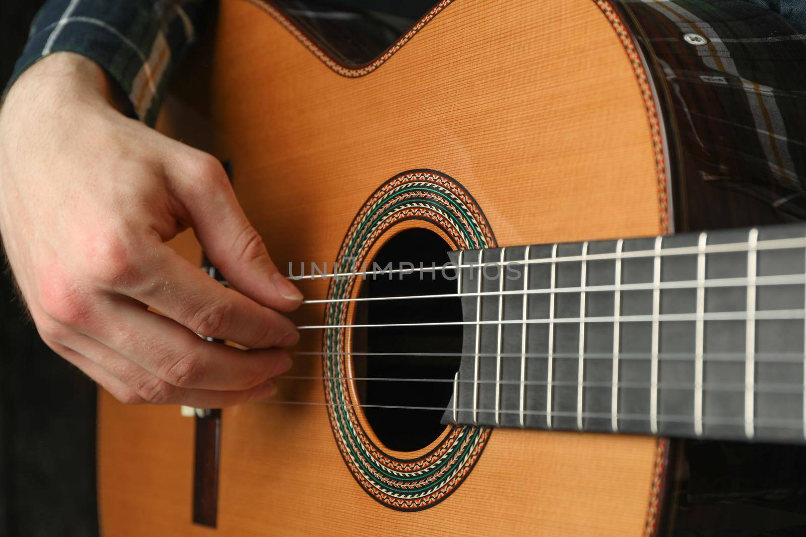 Man playing on classic guitar against dark background, space for text