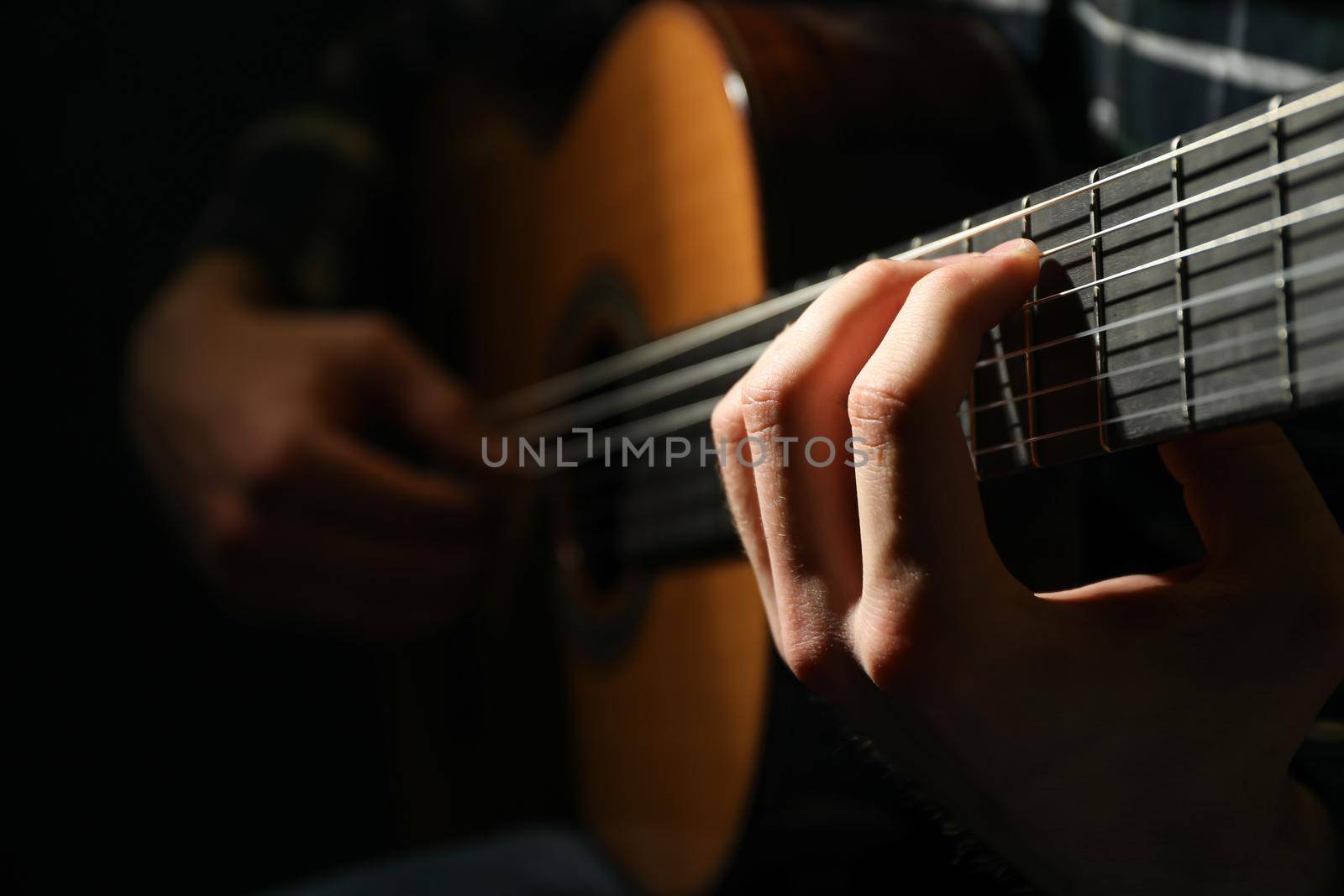 Man playing on classic guitar against dark background, closeup