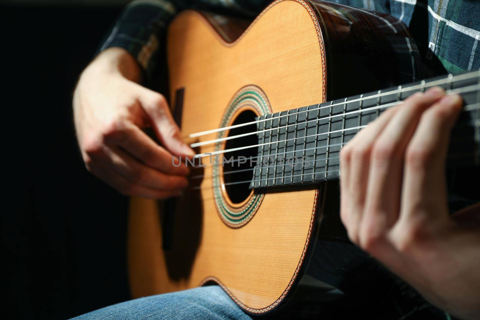 Man playing on classic guitar against dark background, closeup by AtlasCompany