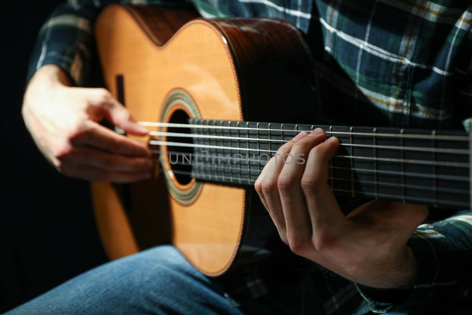 Man playing on classic guitar against dark background, closeup by AtlasCompany