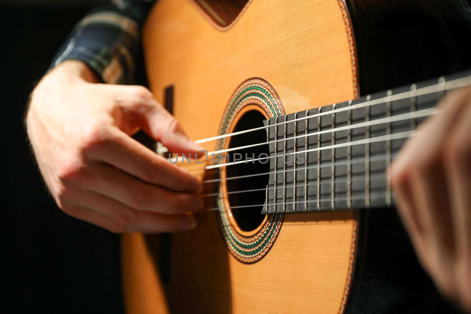 Man playing on classic guitar against dark background, closeup