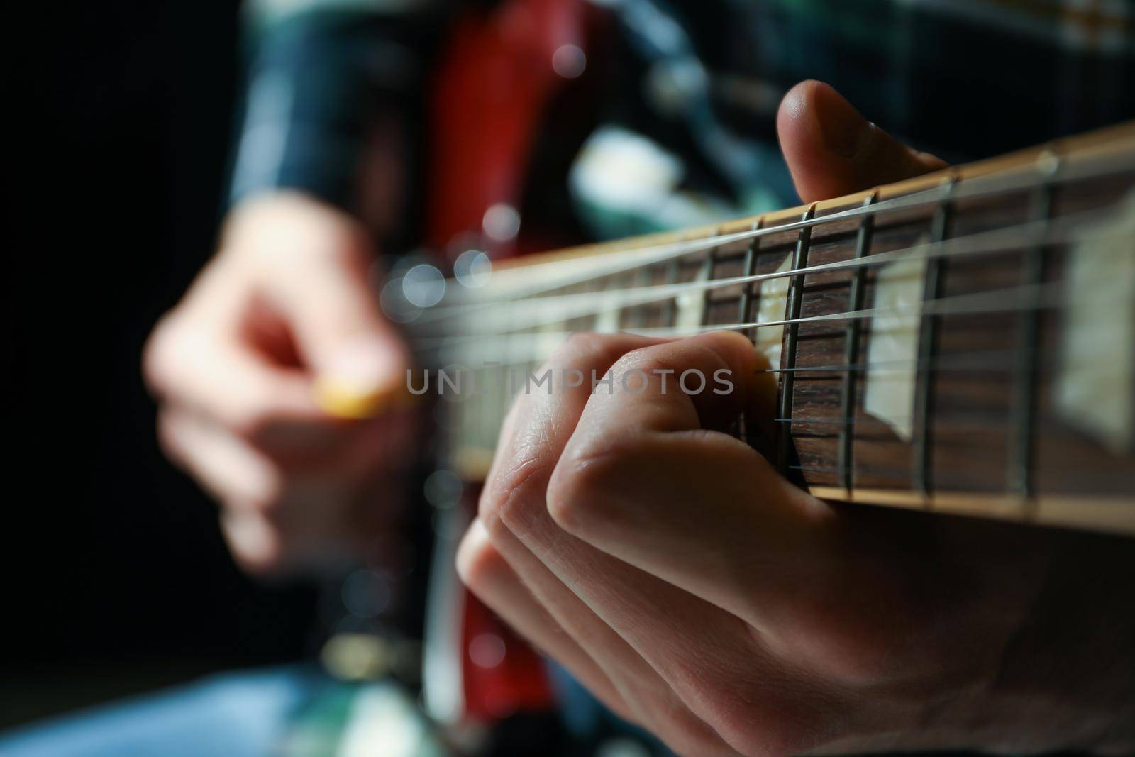 Man playing on electric guitar against dark background, closeup by AtlasCompany