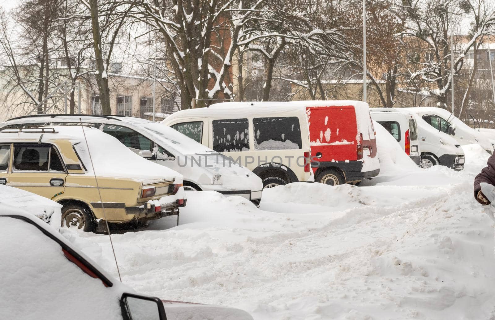 Stuck cars under the snow and ice. City street after blizzard. Buried vehicle in snowdrift on the road. Parking lots in winter after heavy snowfall. Uncleaned roads. Record-breaking amounts of snow.