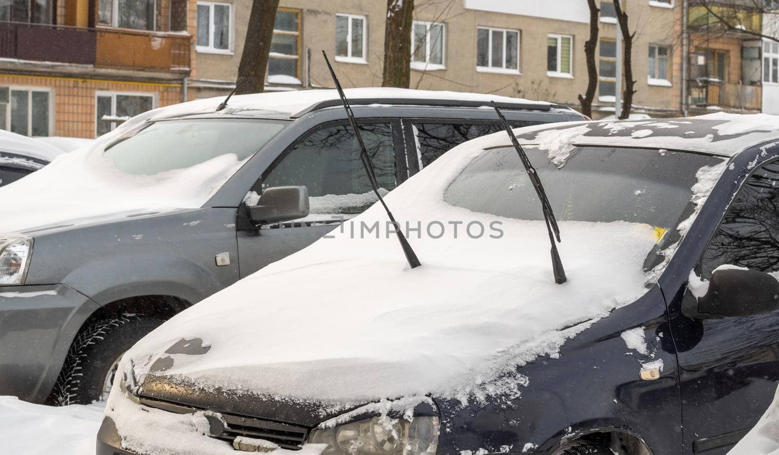 Stuck cars under the snow and ice. City street after blizzard. Buried vehicle in snowdrift on the road. Parking lots in winter after heavy snowfall. Uncleaned roads. Record-breaking amounts of snow.