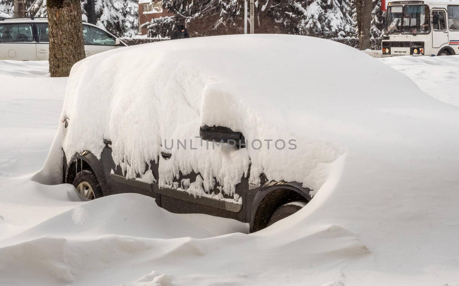 Stuck cars under the snow and ice. City street after blizzard. Buried vehicle in snowdrift on the road. Parking lots in winter after heavy snowfall. Uncleaned roads. Record-breaking amounts of snow.
