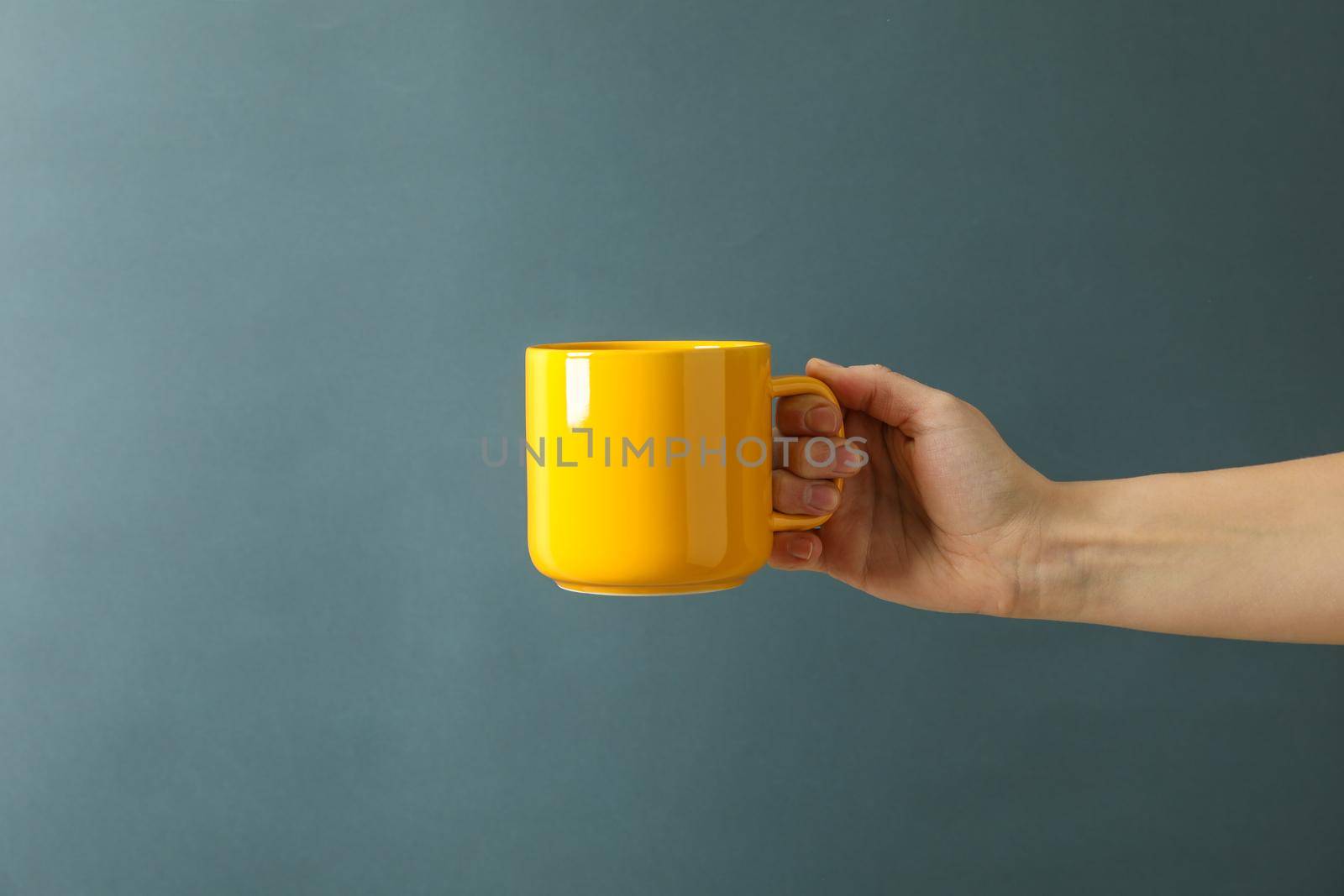 Female hand hold yellow cup against black background, space for text