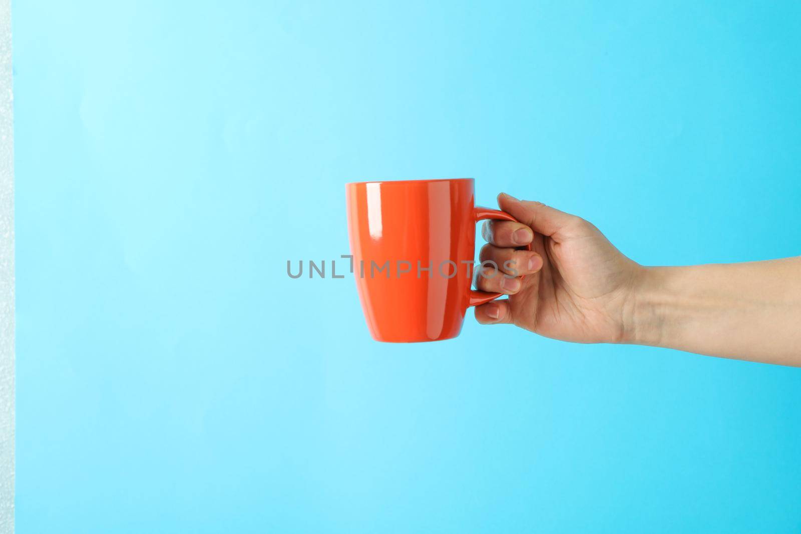 Female hand holding red cup against color background, space for text