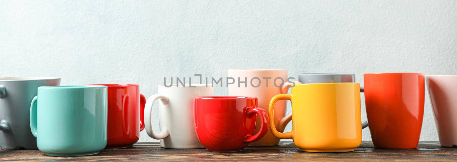 Multicolored cups on wooden table against light background, space for text