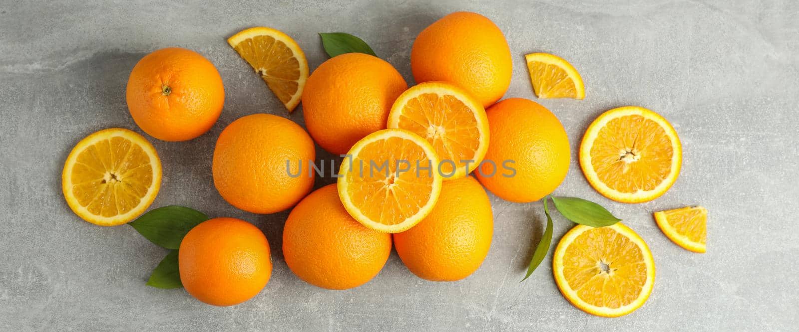 Many ripe oranges with leaves on grey table, top view