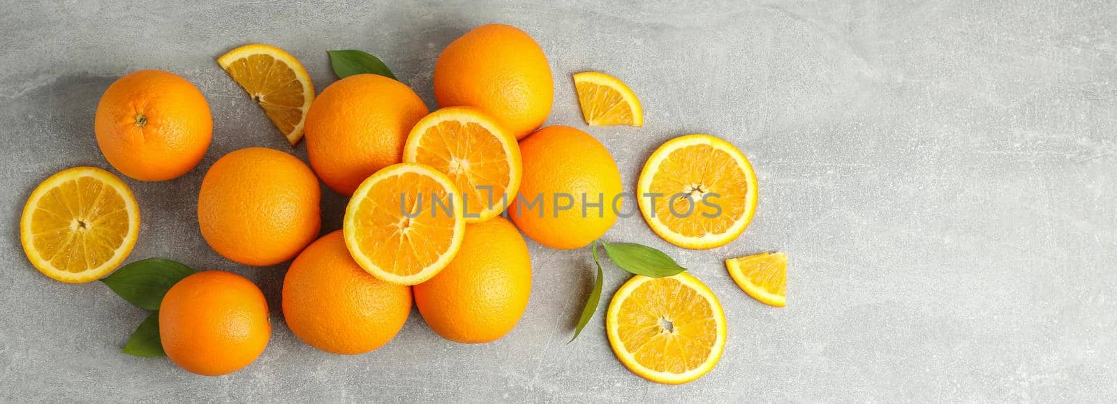 Many ripe oranges with leaves on grey table, top view