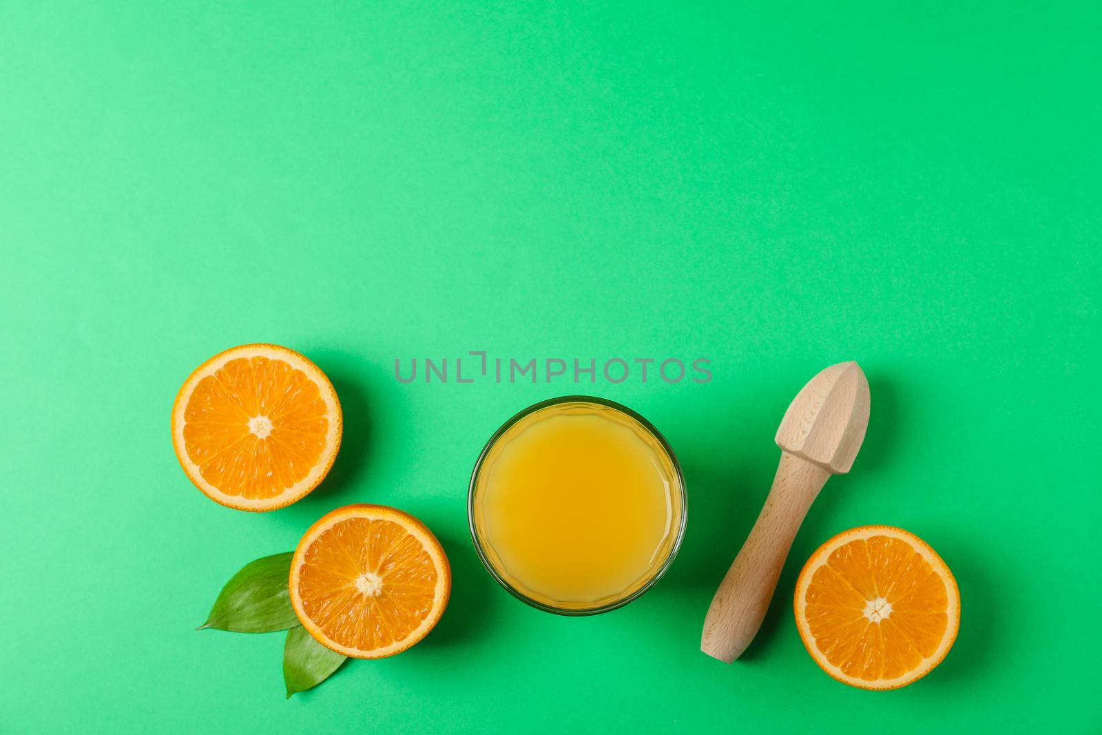 Flat lay composition with fresh orange juice, wooden juicer and oranges with leaves on color background, space for text. Fresh natural drink