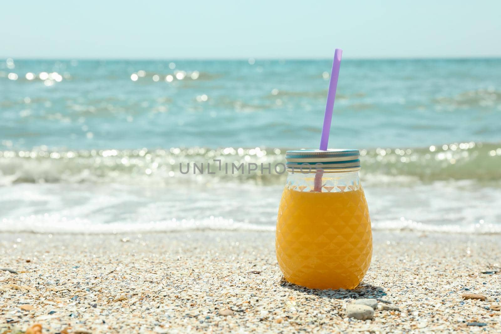 Glass jar of fresh orange juice on seaside, space for text. Summer vacation background