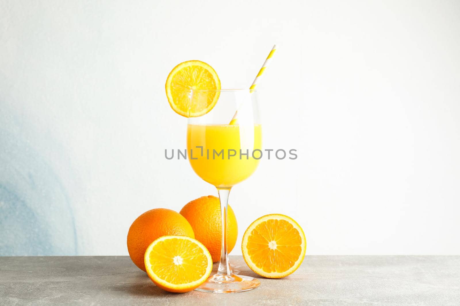 Glass with fresh orange juice and tubule, oranges on grey table against color background, space for text. Fresh natural drink by AtlasCompany