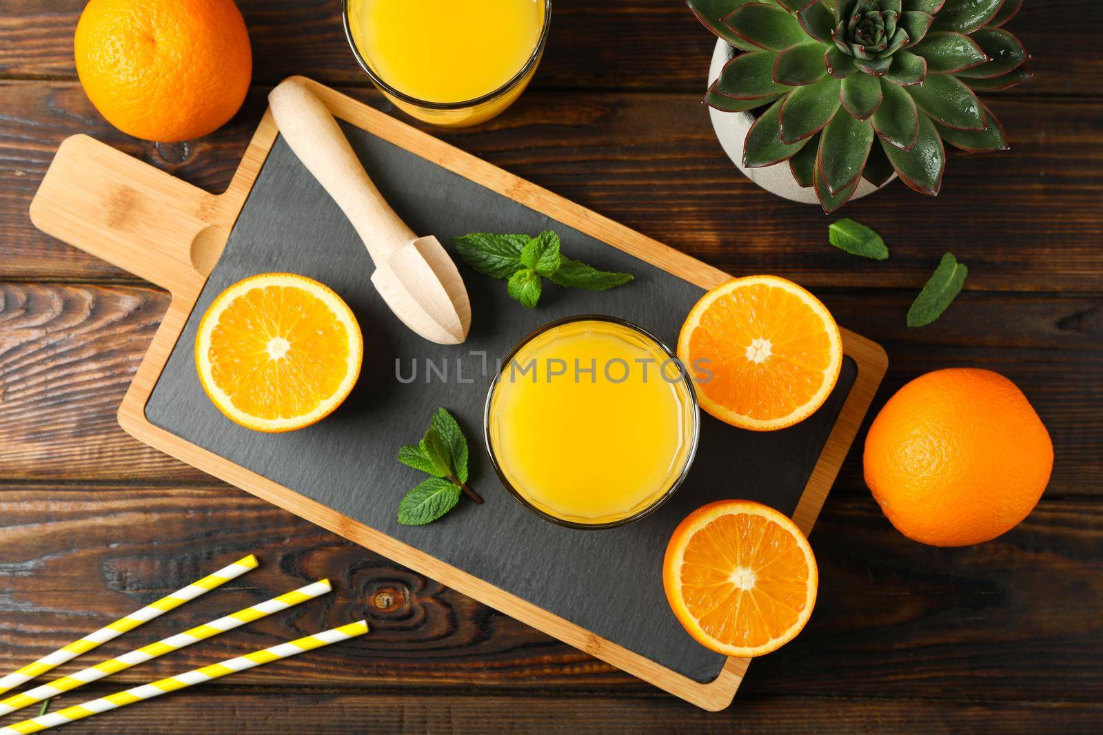 Cutting board, orange juice, wooden juicer, mint, orange, tubule and succulent plant on wooden table, top view. Fresh natural drink and fruits