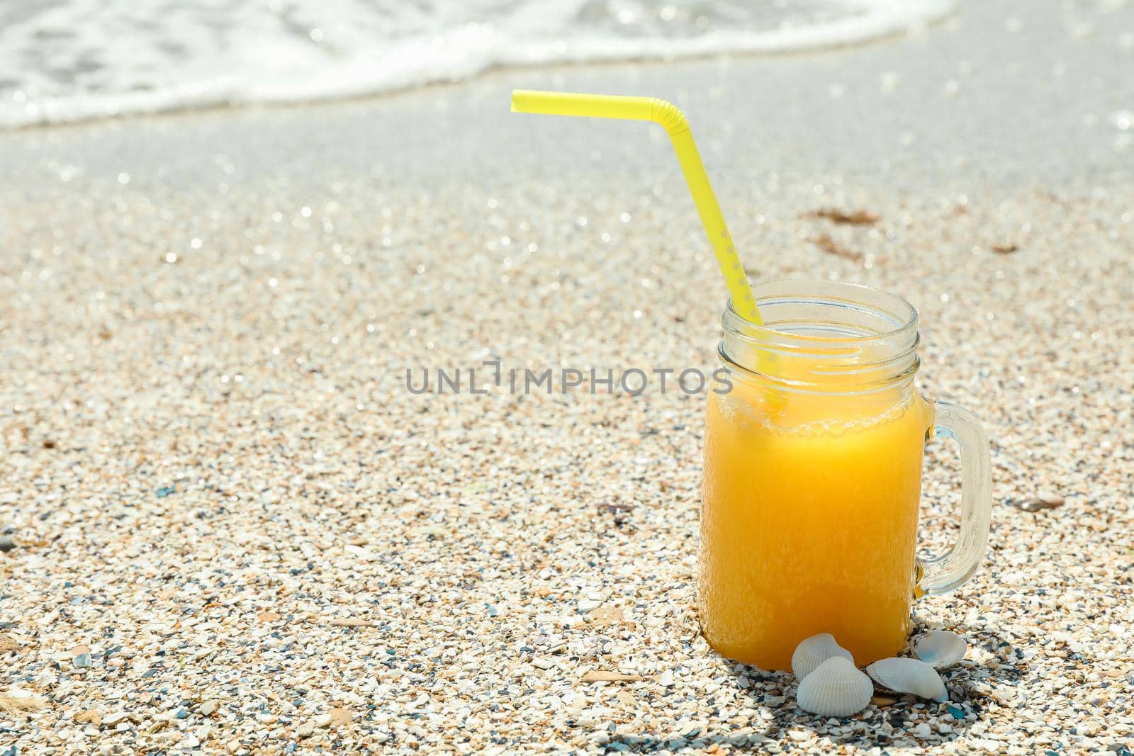 Glass jar of fresh orange juice on seaside, space for text. Summer vacation background