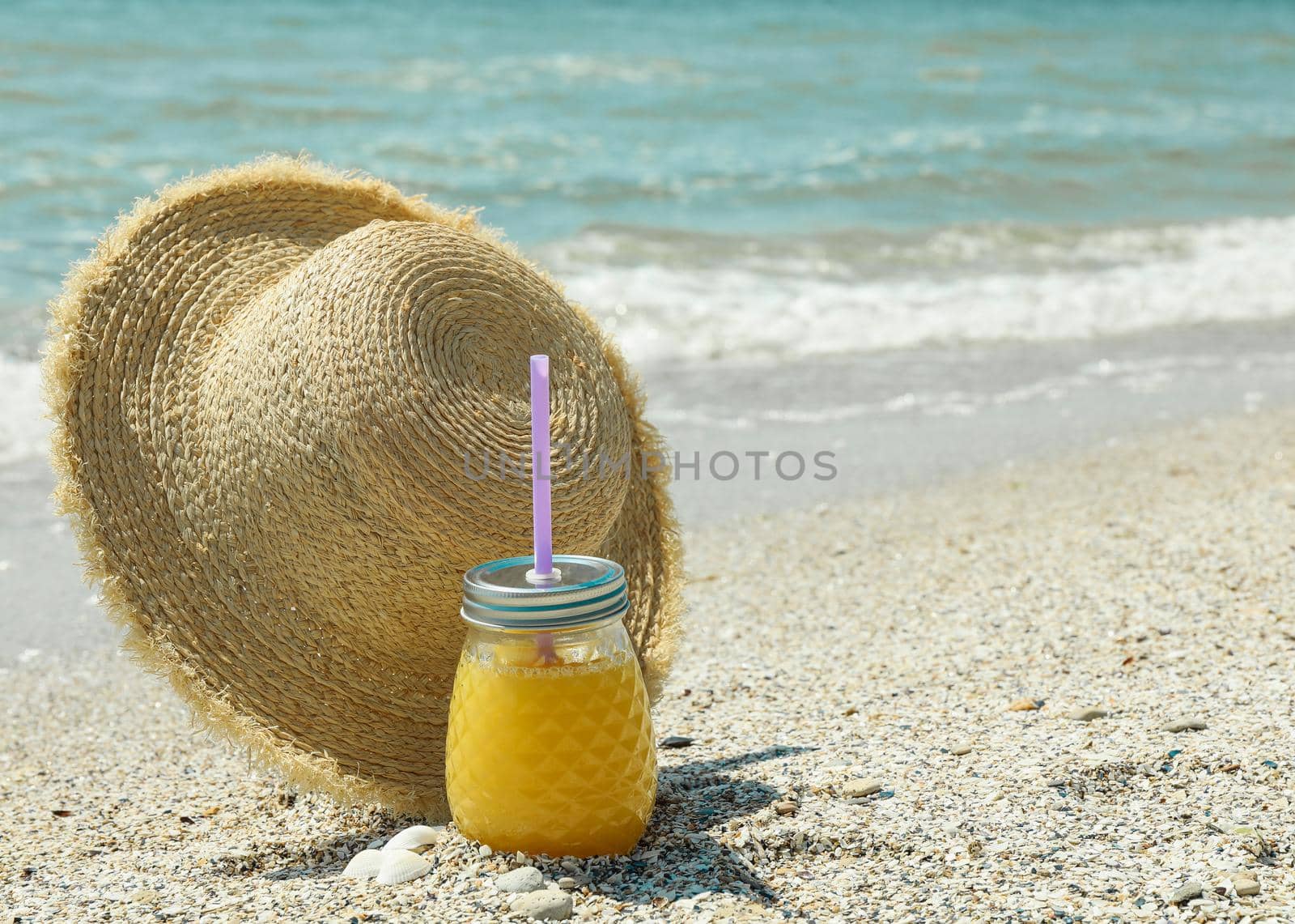 Straw hat and orange juice on seaside, space for text. Summer vacation background