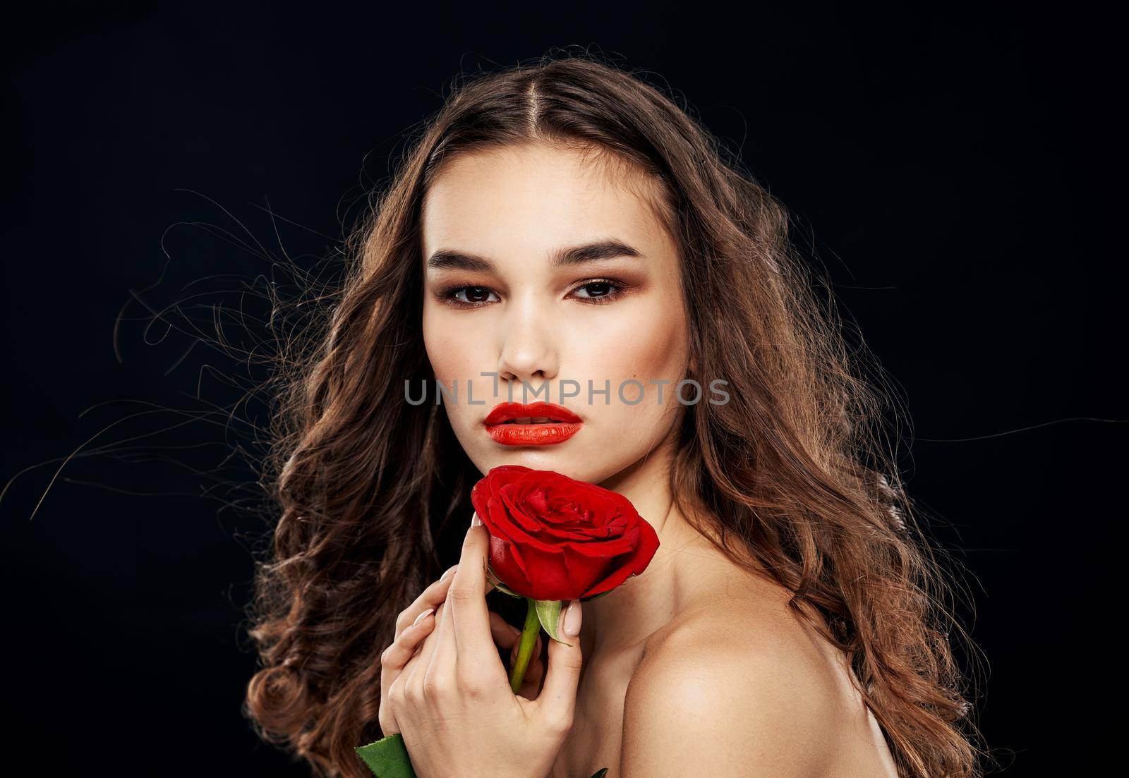 Brunette woman with a red rose in her hand on a dark background close-up by SHOTPRIME