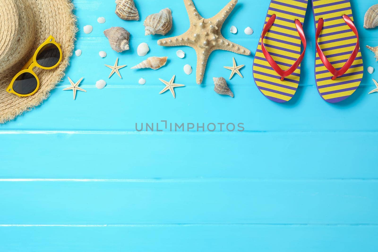 Straw hat, sunglasses, flip flops and many starfishes on color wooden background, space for text and top view. Summer vacation backdrop by AtlasCompany