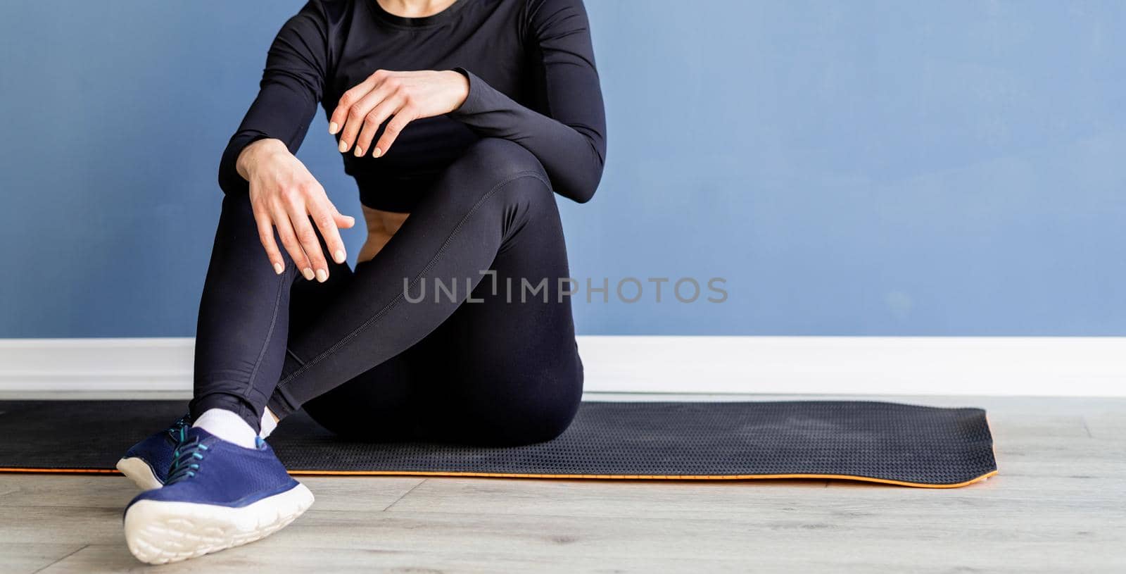 Fitness, sport and technology. Young athletic woman wearing virtual reality glasses sitting at fitness mat at blue background