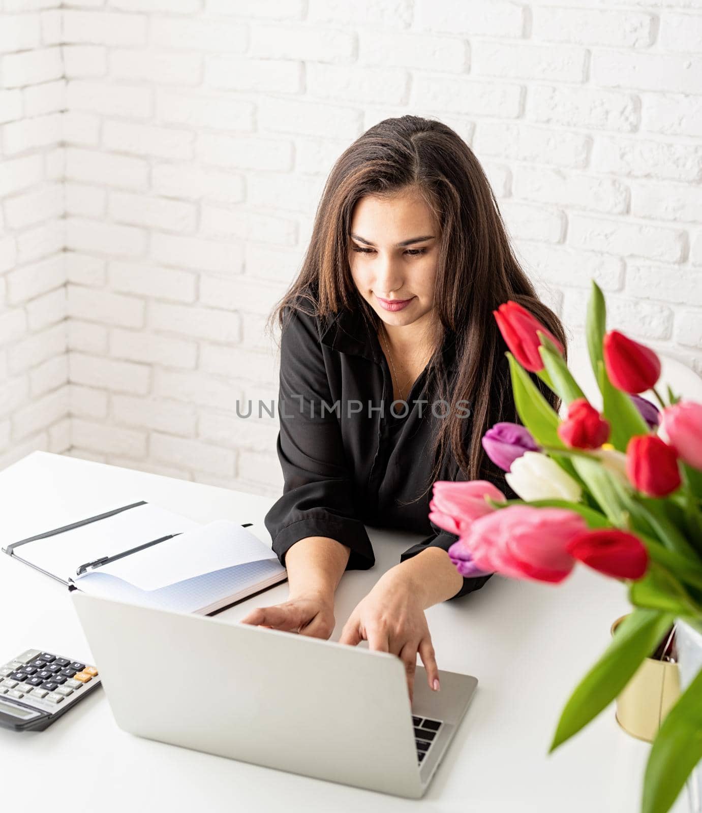 young brunette business woman florist using laptop in the office, bucket of tulips on the desk. Small business.