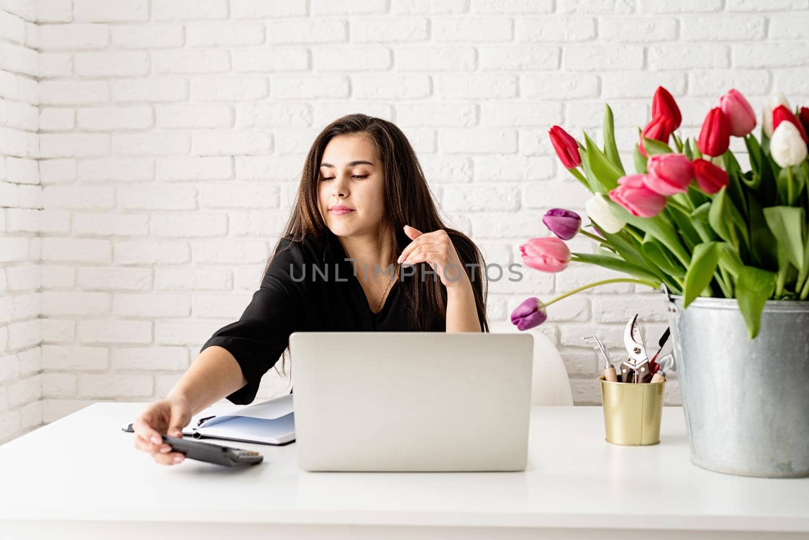 young brunette business woman florist working in the office, calculating costs, bucket of tulips on the desk. Small business.