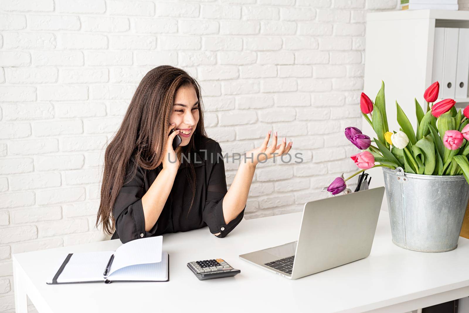 Small business concept. Young brunette business woman florist Talking on the phone, working at the office, bucket of tulips on the desk