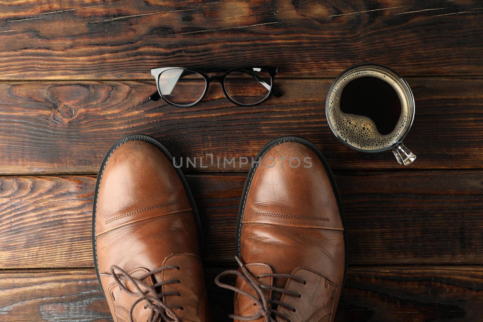 Brown leather shoes, cup of coffee and glasses on wooden background, space for text and top view