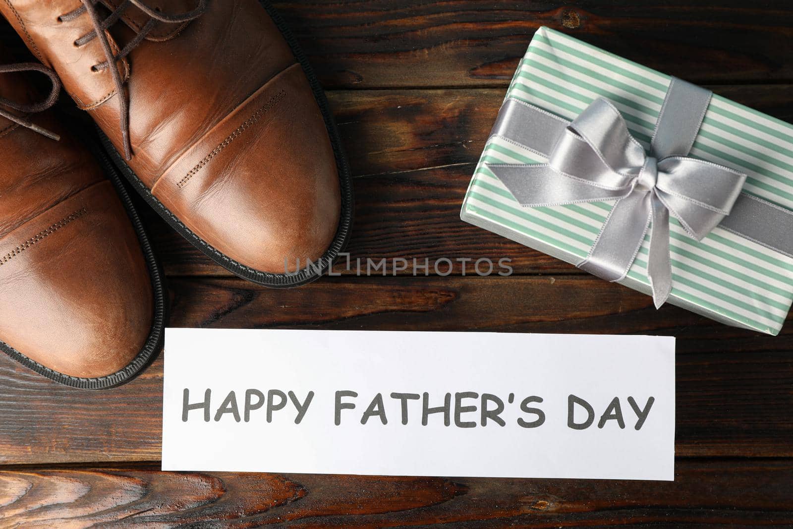 Brown leather shoes, inscription happy fathers day and gift box on wooden background, space for text and top view