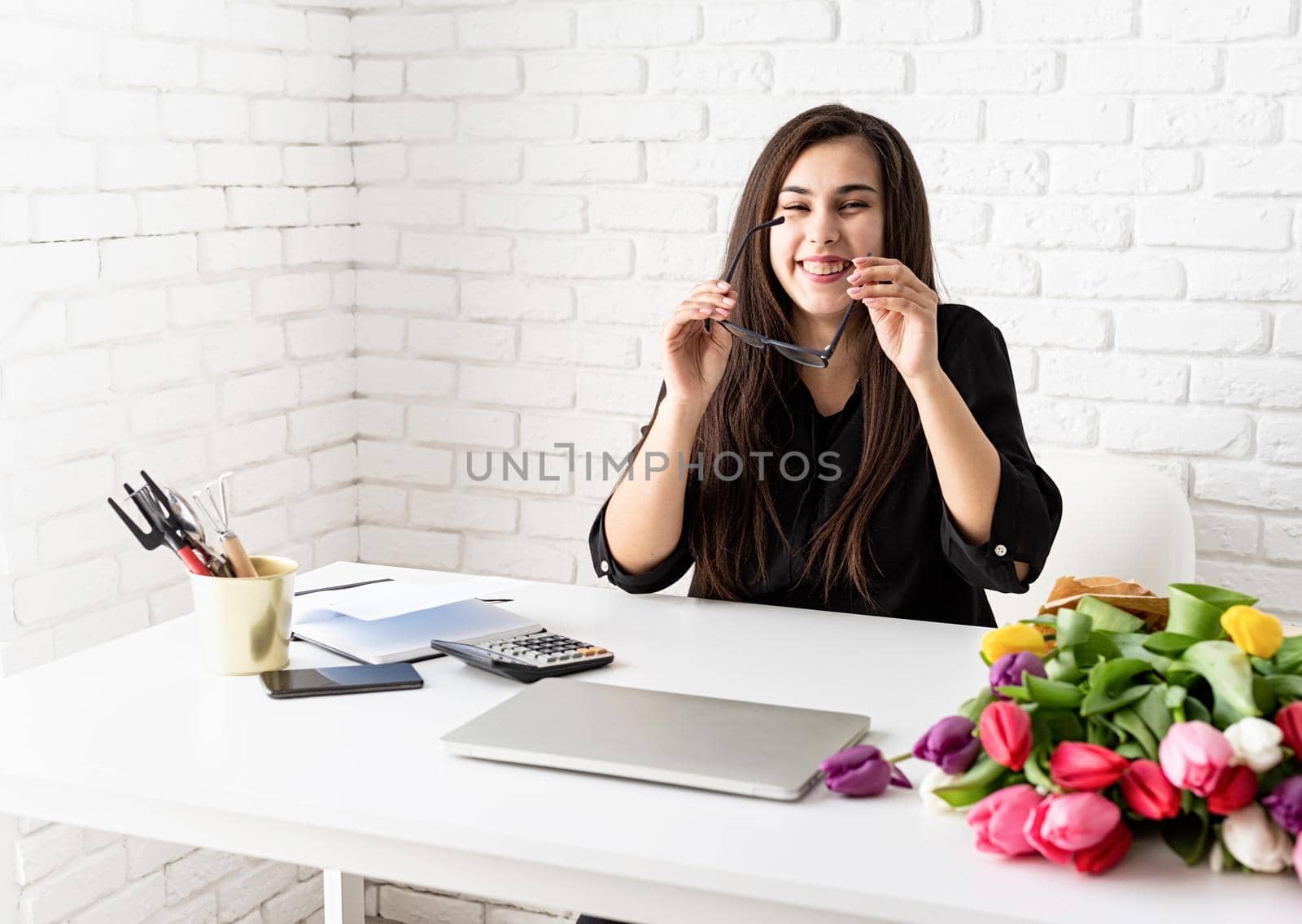 Small business concept. A young laughing business woman florist working on a laptop in the office putting on glasses
