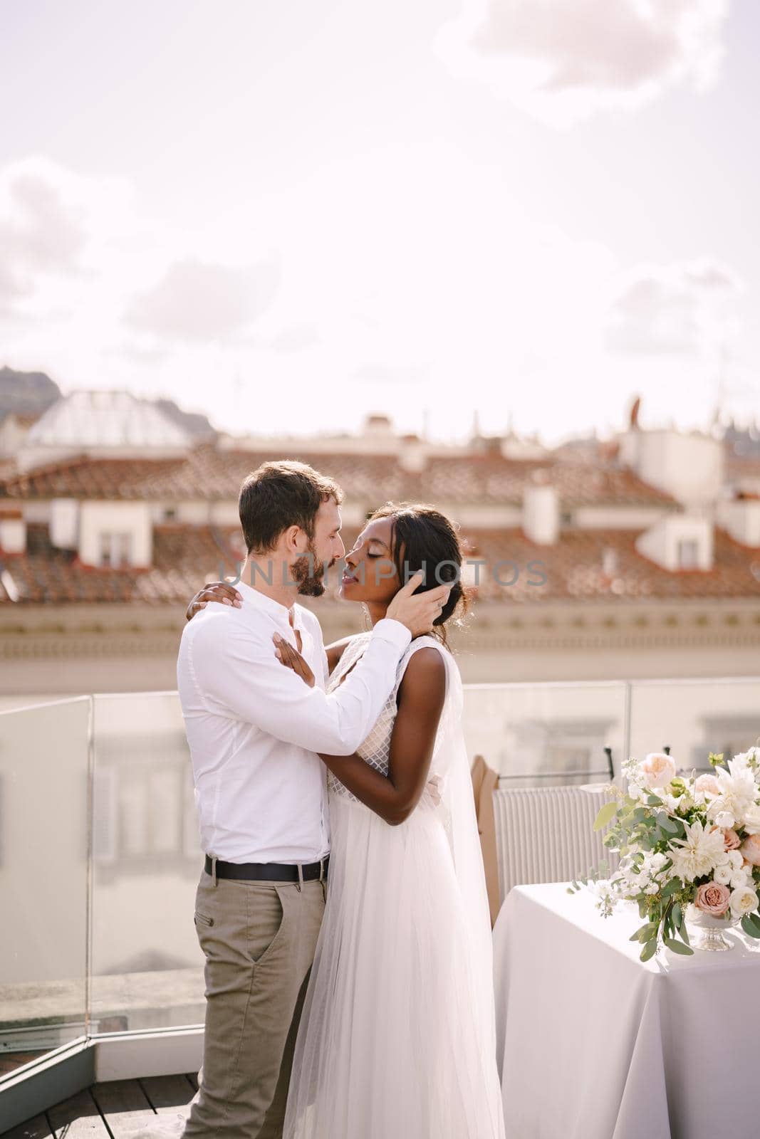 Destination fine-art wedding in Florence, Italy. Mixed-race wedding couple. African-American bride and Caucasian groom stand near the table for a wedding dinner. by Nadtochiy