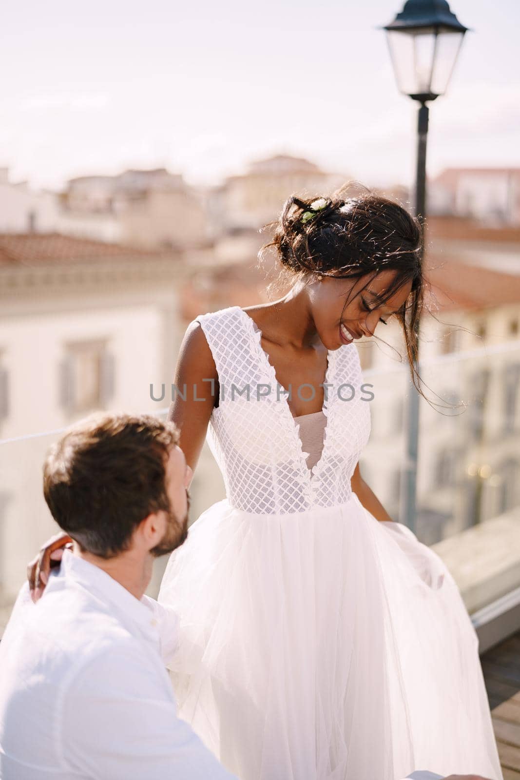 Interracial wedding couple. Destination fine-art wedding in Florence, Italy. African-American bride and Caucasian groom dance near the table for a wedding dinner, on the roof of the restaurant.