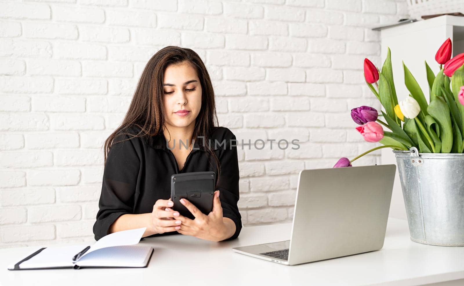 young brunette business woman florist working in the office, calculating costs, bucket of tulips on the desk. Small business.