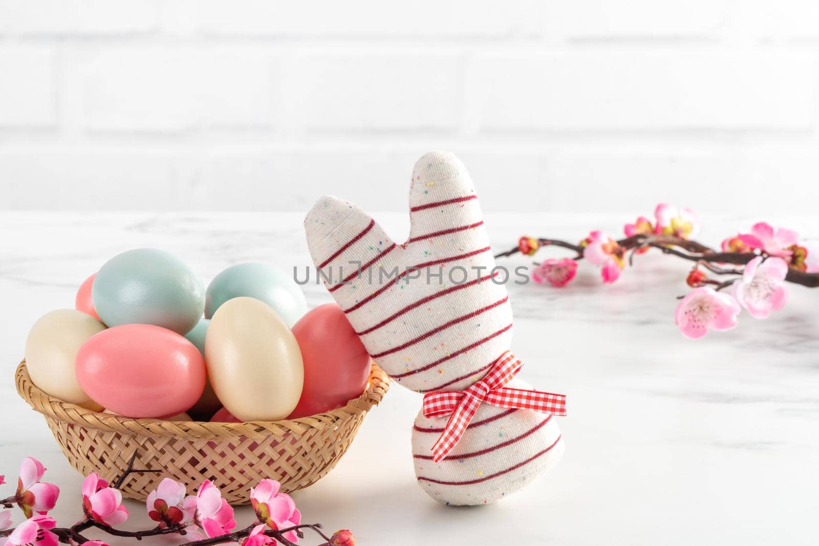 Close up of colorful Easter eggs in the nest with pink plum flower on bright white wooden table background.