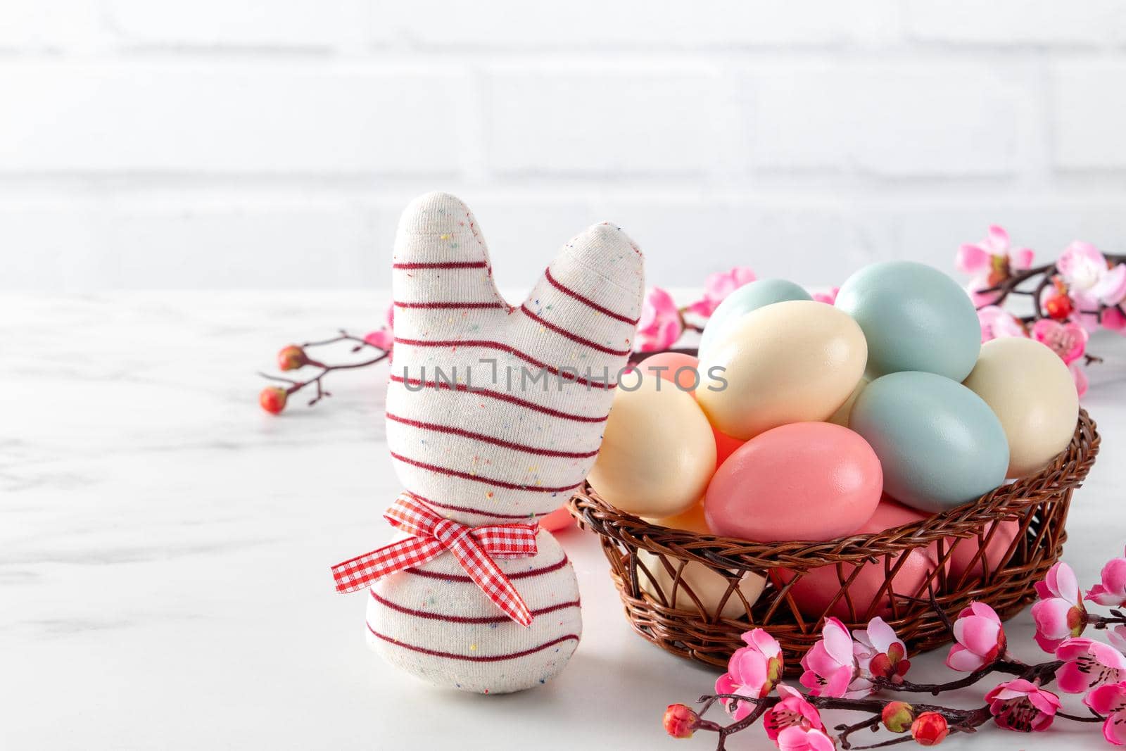 Close up of colorful Easter eggs in the nest with pink plum flower on bright white wooden table background.