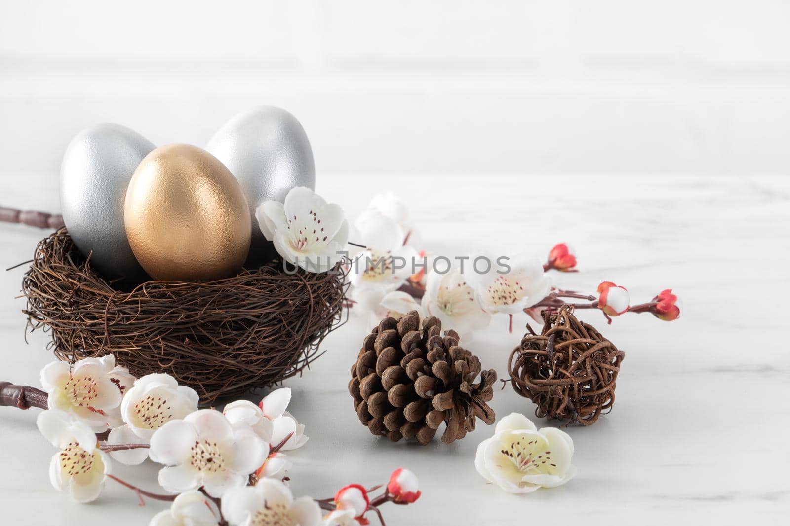 Close up of golden and silver Easter eggs in the nest with white plum flower. by ROMIXIMAGE