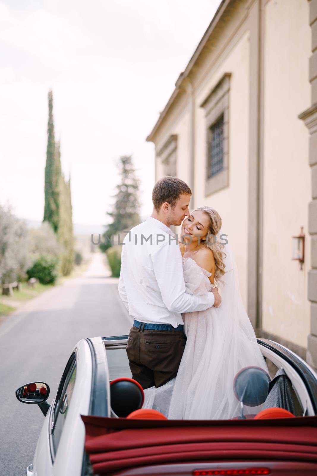 Wedding in Florence, Italy, in an old villa-winery. The bride and groom kiss in an open convertible.