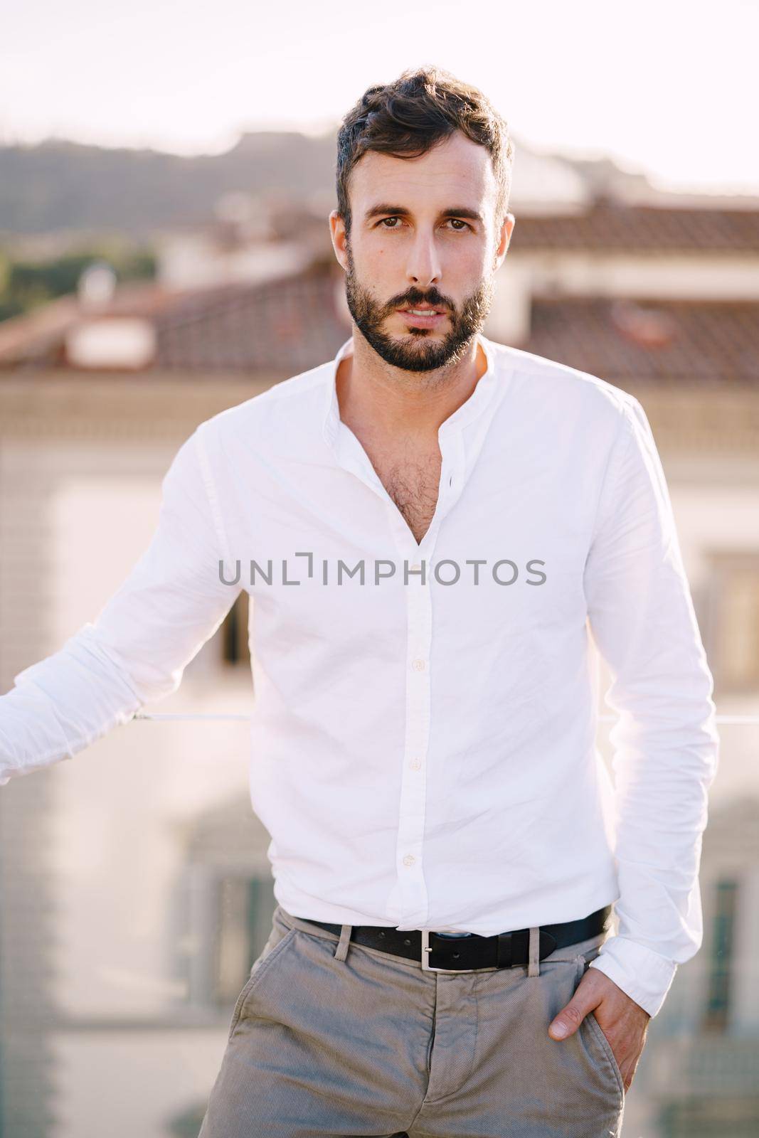 Stylish bearded guy in white shirt and light trousers on a rooftop terrace in Florence, Italy