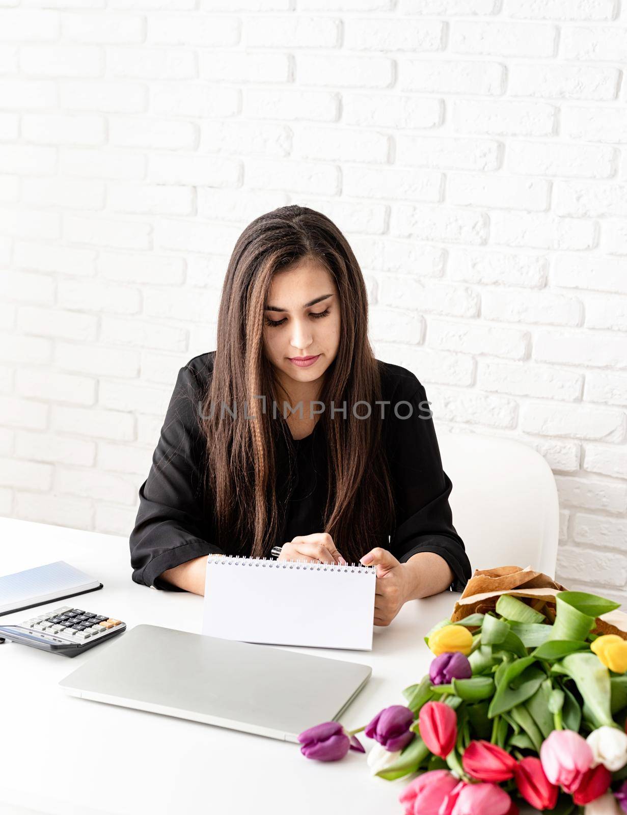 Small business concept. Spring holidays. Business woman making notes in blank desk calendar, working with flowers at the office. Mock up design