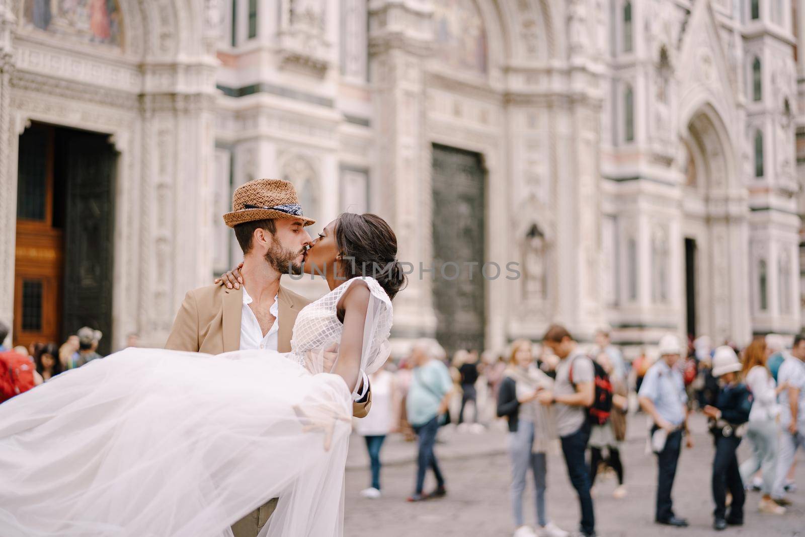 Caucasian groom circles and kisses African-American bride in Piazza del Duomo. Wedding in Florence, Italy. Mixed-race wedding couple