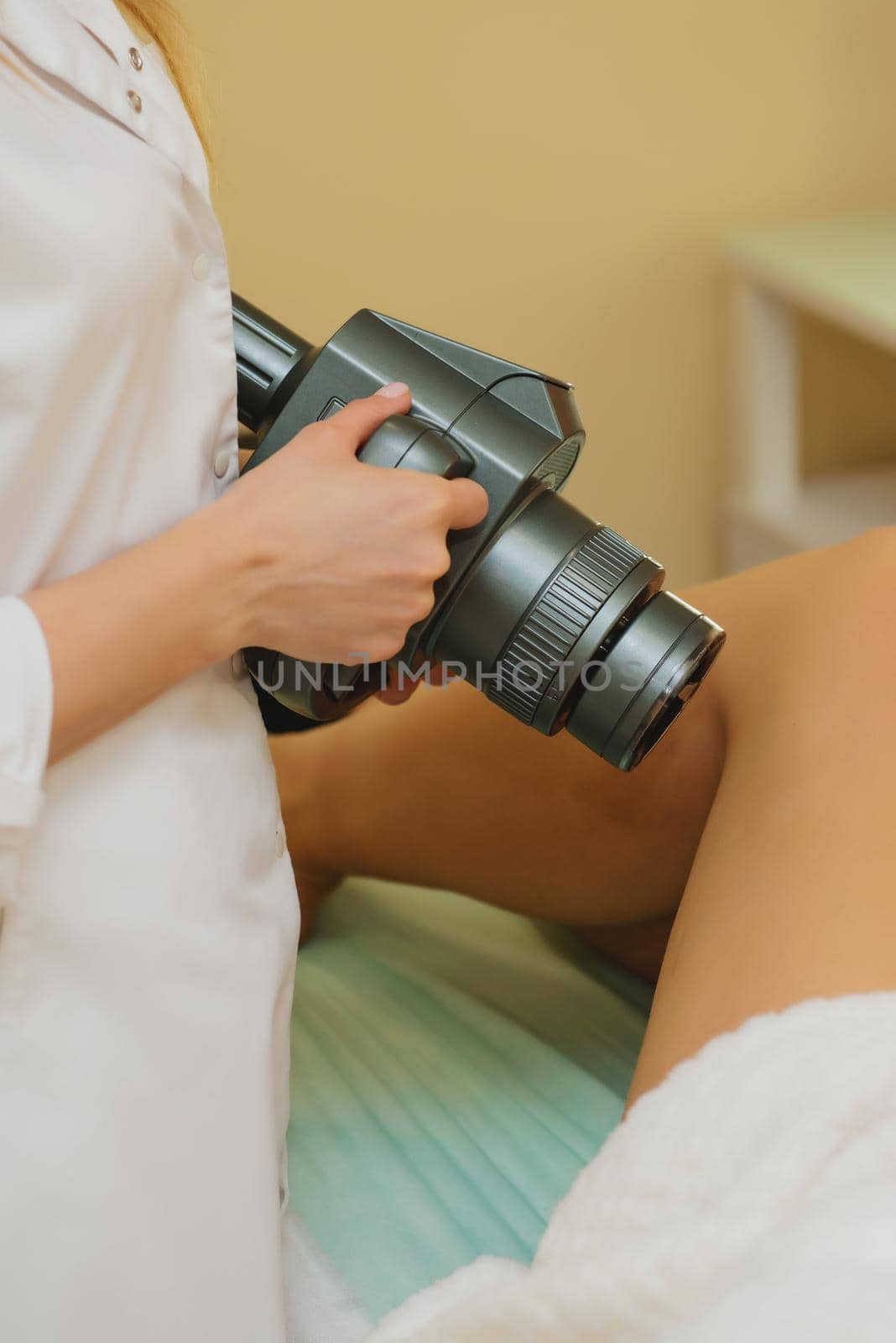 Cosmetologist doing massage with apparatus on female client legs, close up.