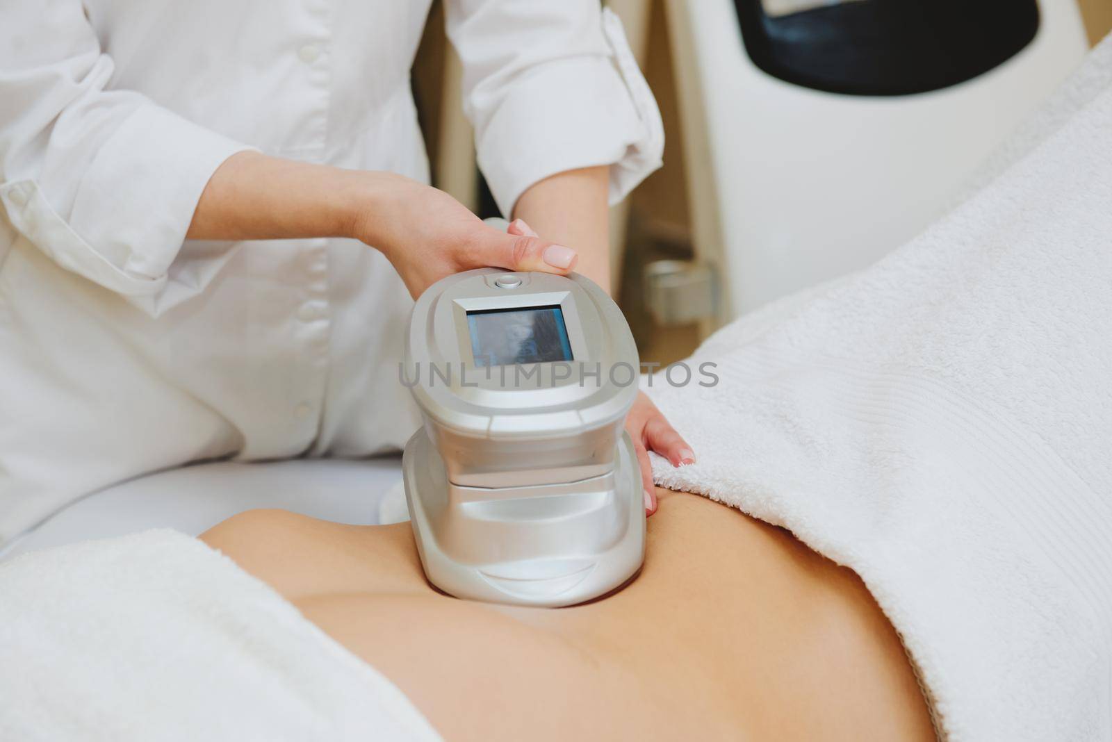 Close-up of cosmetologist doing massage with special apparatus on female belly.