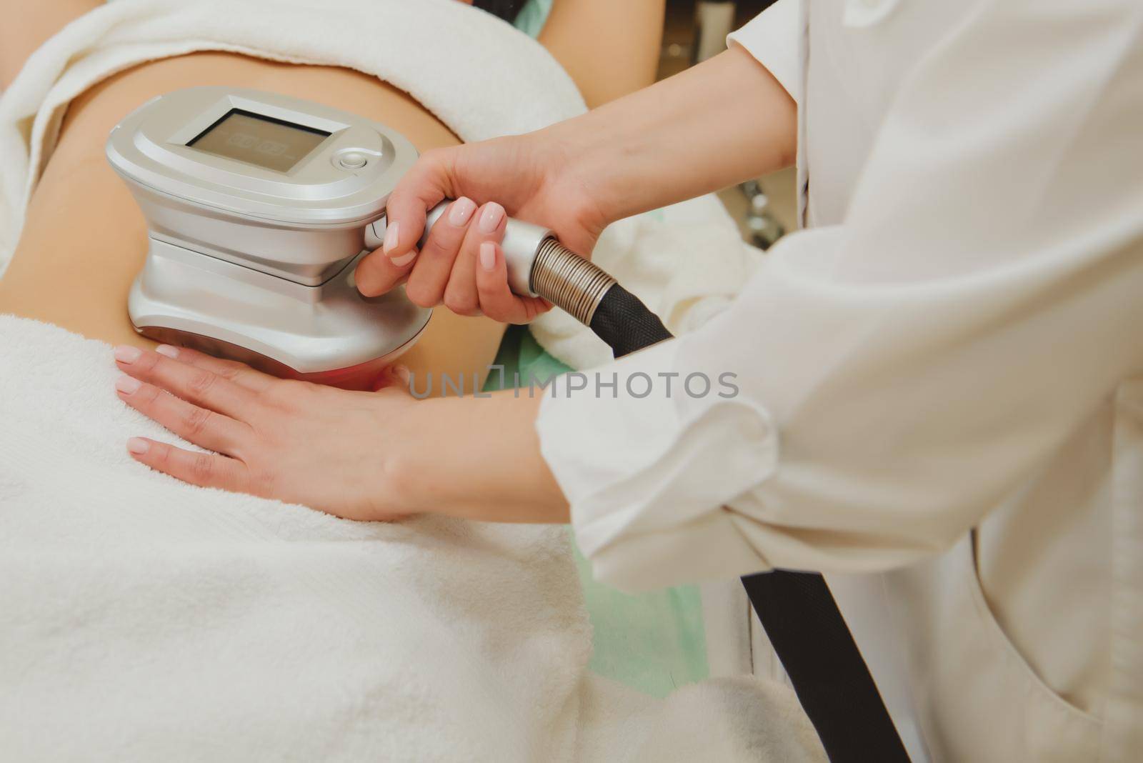 Close-up of cosmetologist doing massage with special apparatus on female belly.