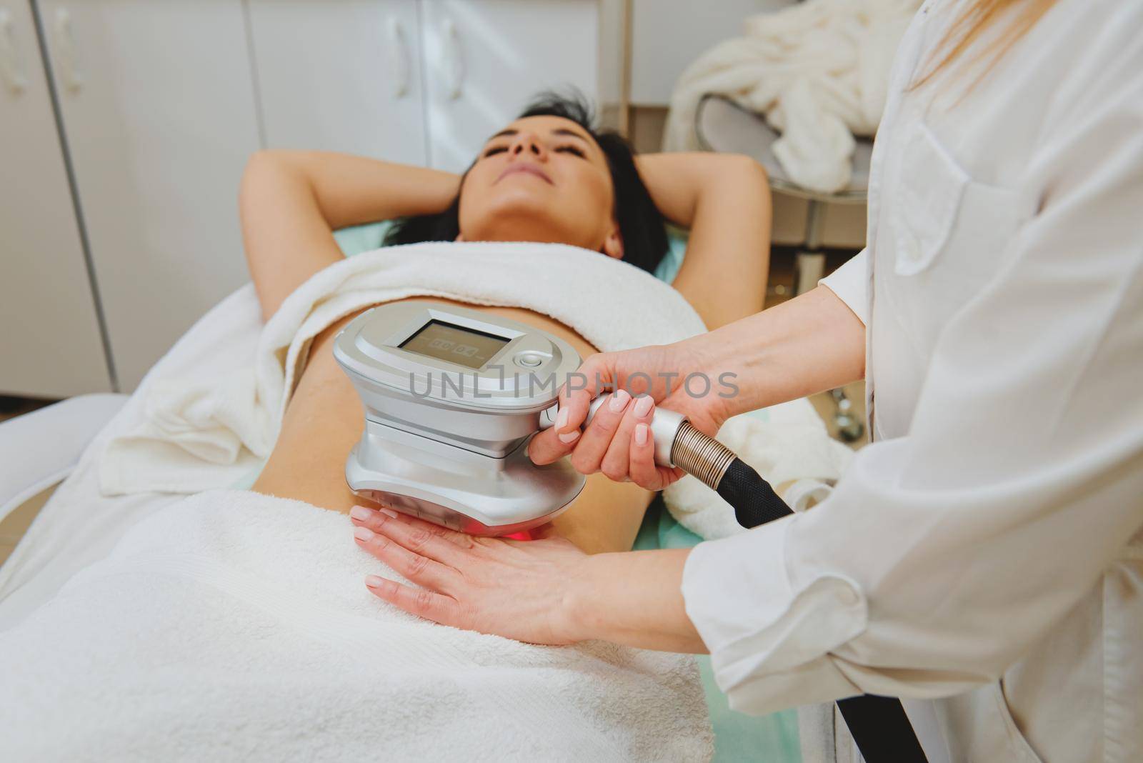 Cosmetologist doing massage with special apparatus on female belly.