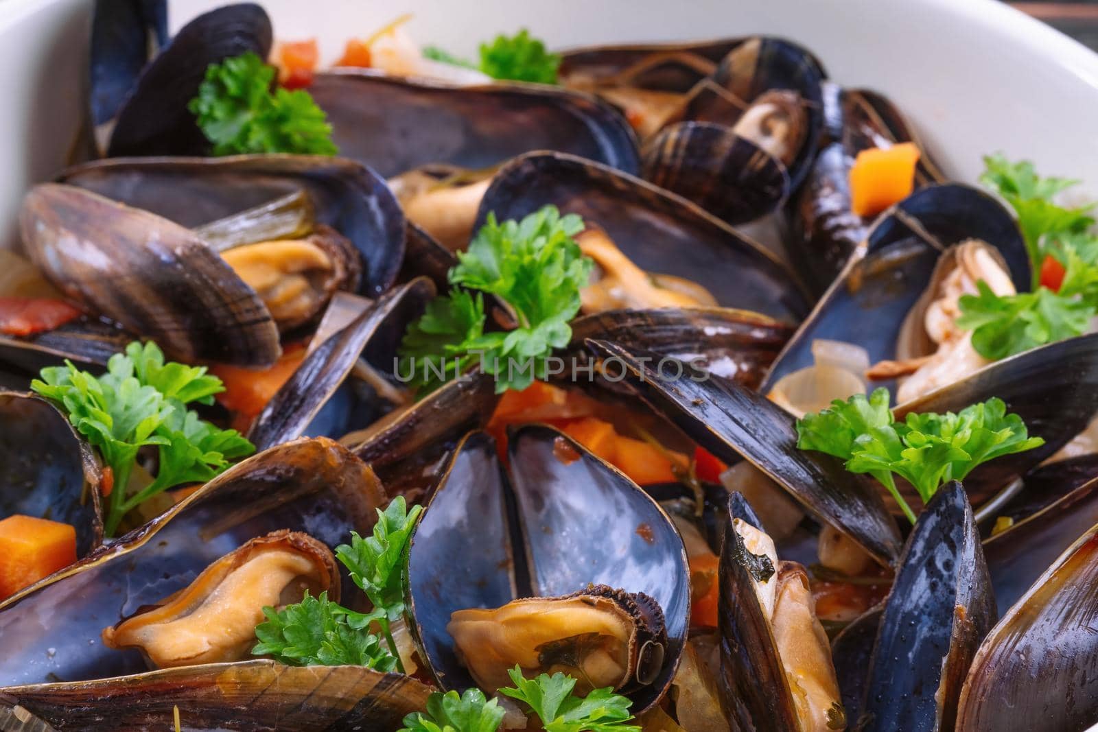 Boiled mussels in cooking dish with parsley on dark wooden background