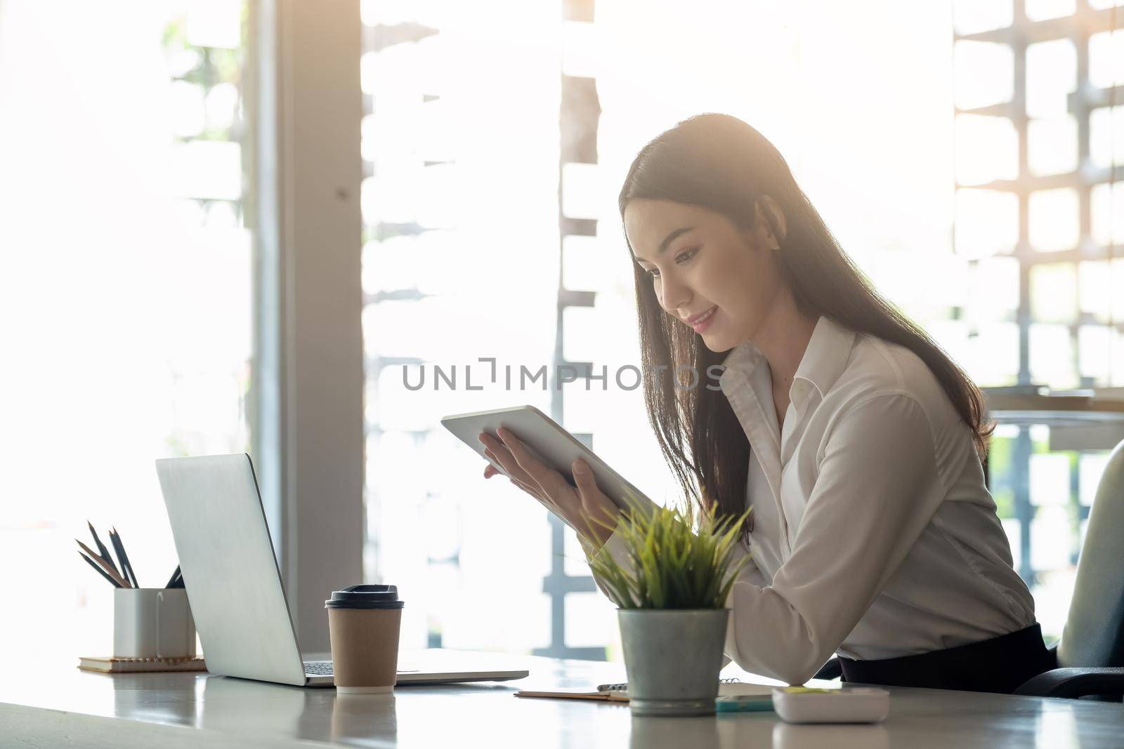 Beautiful business woman uses tablet and laptop while working in the office. by nateemee